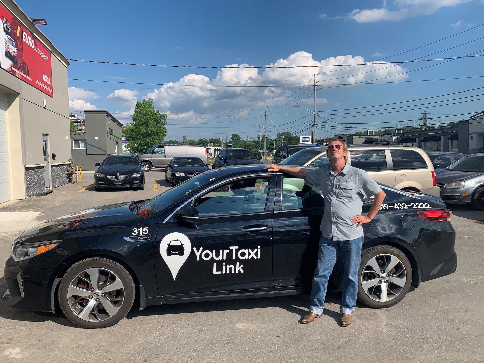 A man is standing next to a black car that says `` your taxi link ''.