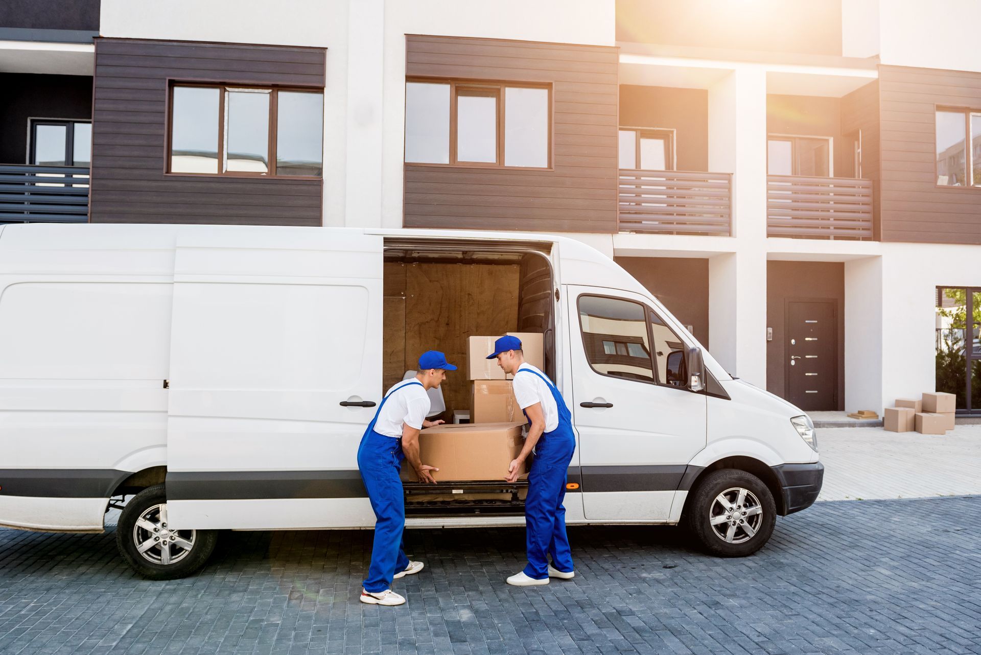 Two men are loading boxes into a van in front of a building.