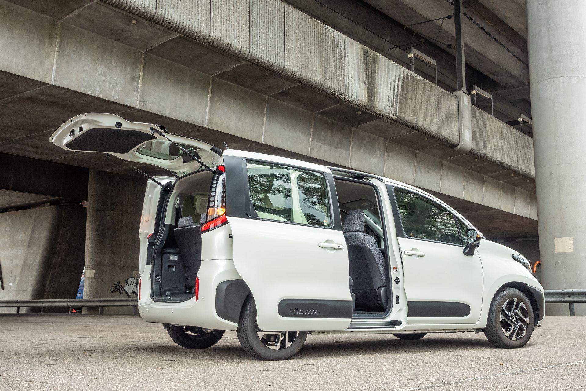 A white van with the trunk open is parked under a bridge.