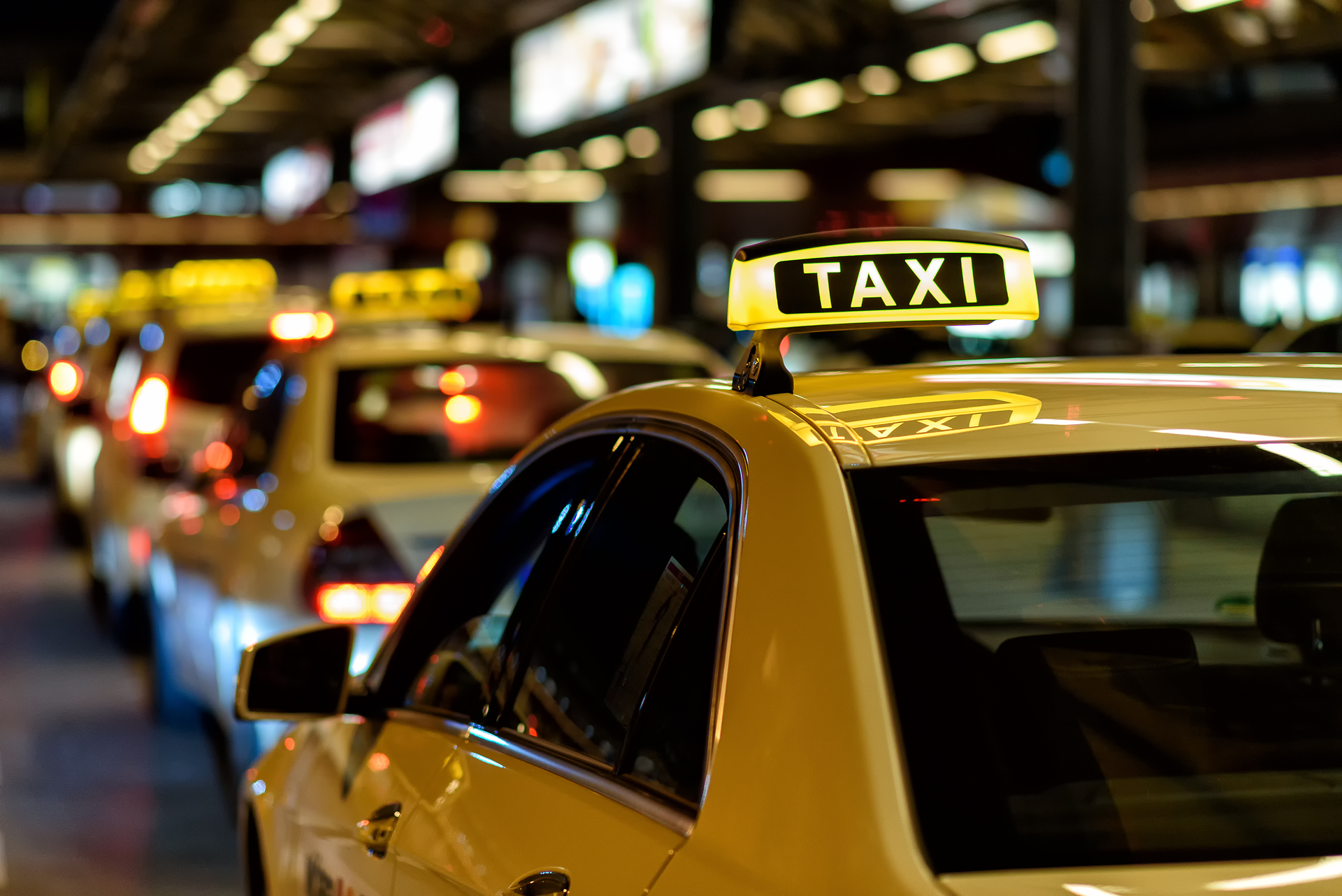 A row of taxi cabs are driving down a city street at night.