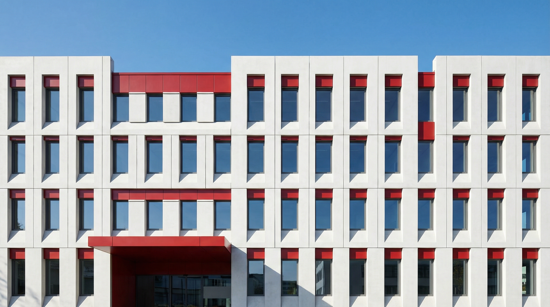 Modern white building facade with red accents and rows of narrow windows