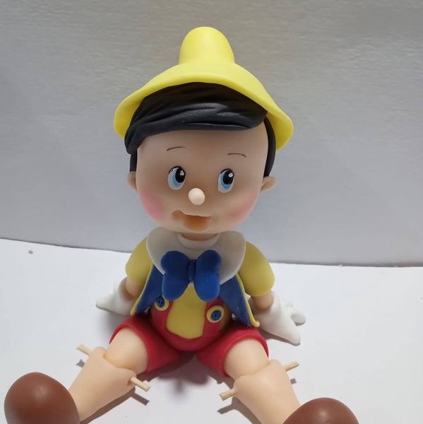 Figura de Pinocho con sombrero amarillo, pajarita azul, pantalones cortos rojos y zapatos marrones.