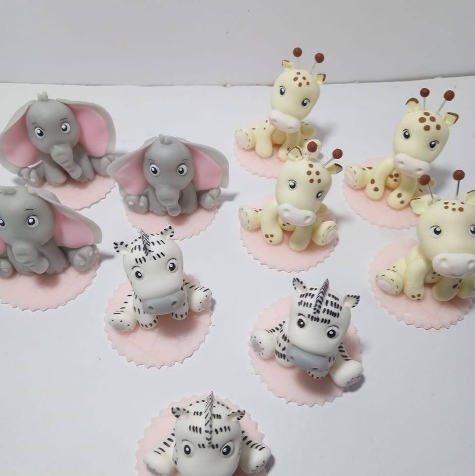 Colección de adornos de fondant para cupcakes con forma de animales: elefantes, jirafas y cebras sobre bases rosas.