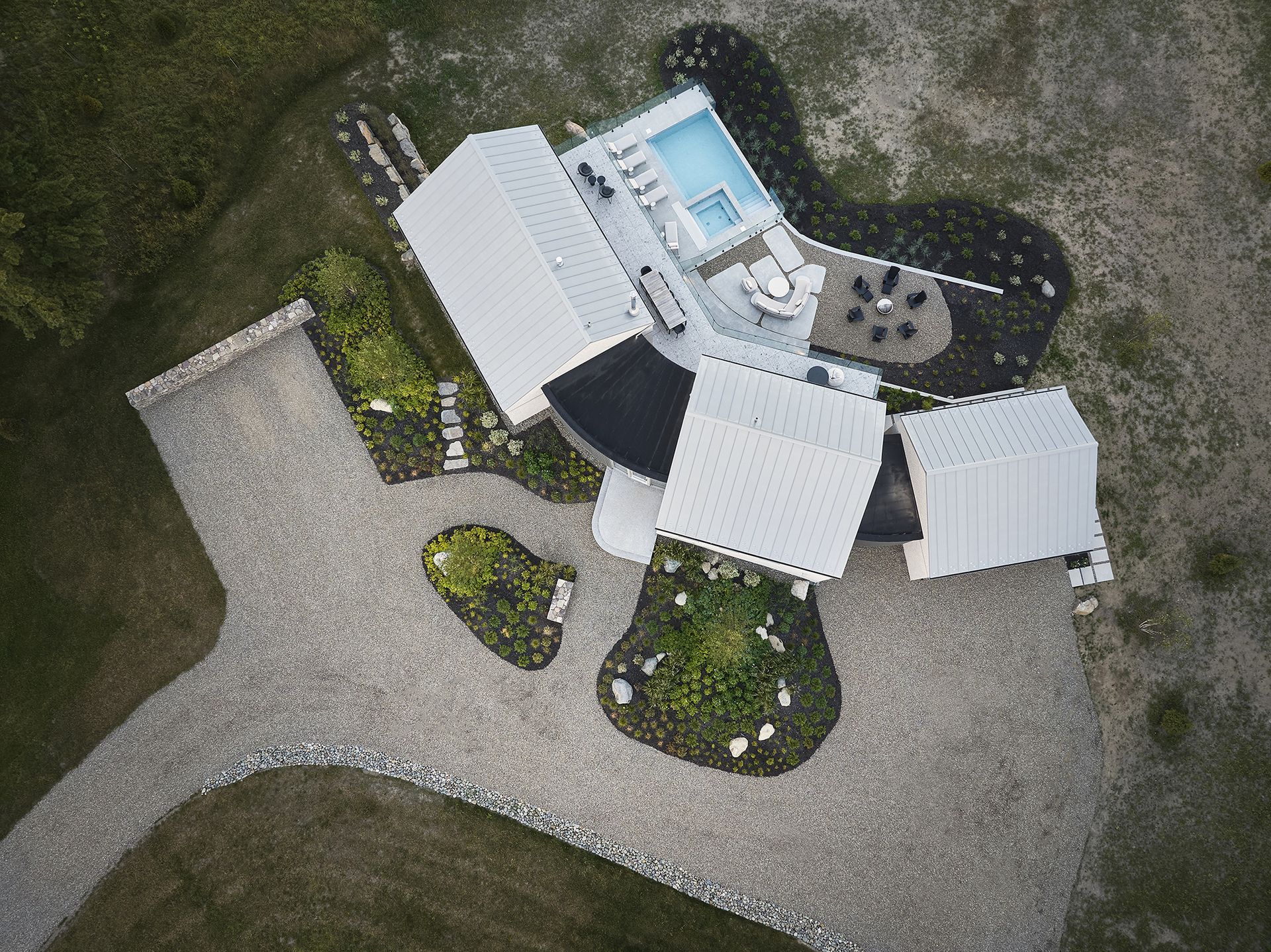 Vue aérienne d'une maison blanche moderne avec piscine, allée de gravier et aménagement paysager environnant.