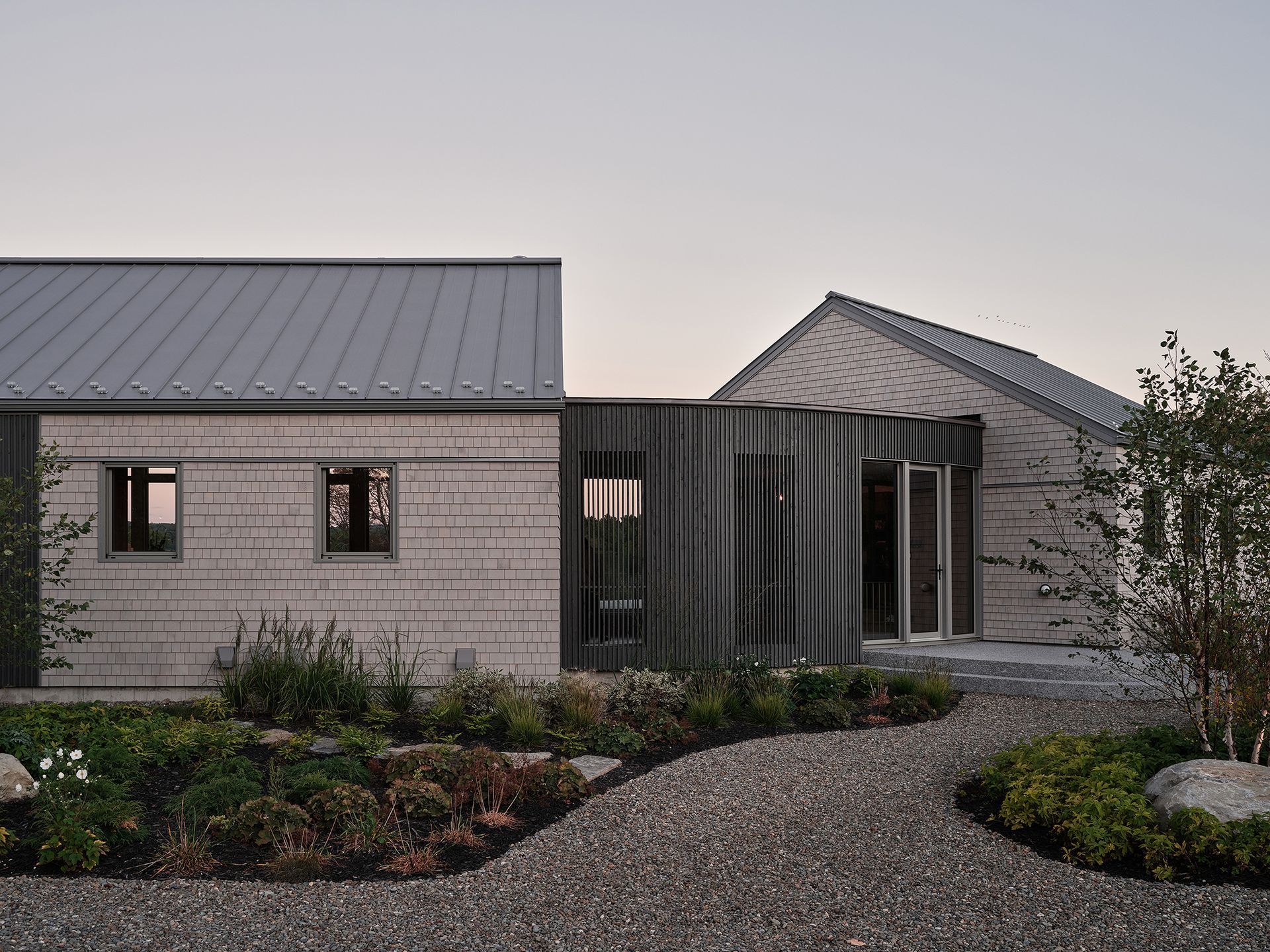Bâtiment gris moderne avec allée de gravier et jardin.
