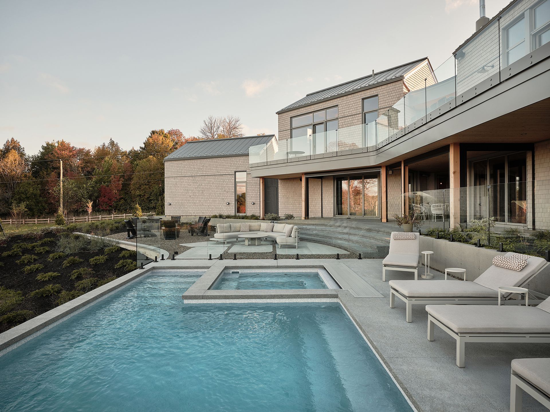 Maison moderne avec piscine et jacuzzi donnant sur un paysage verdoyant ; eau bleue, tons neutres.