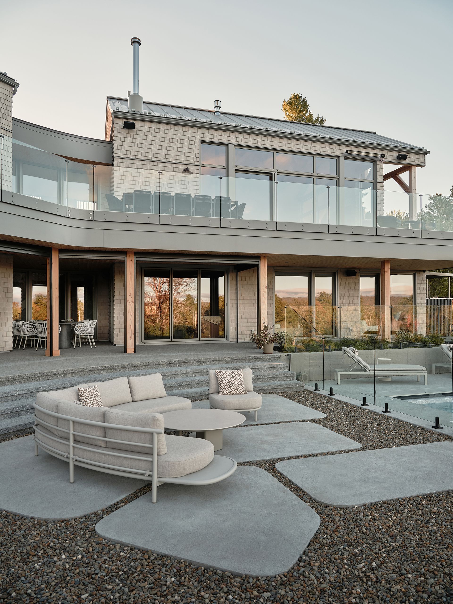 Terrasse extérieure avec sièges incurvés, marches et une maison moderne aux murs de verre.