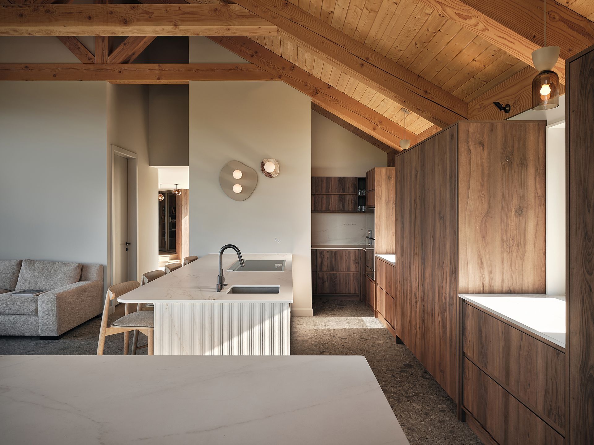 Cuisine avec armoires en bois, comptoirs clairs et poutres apparentes ; lumière naturelle.