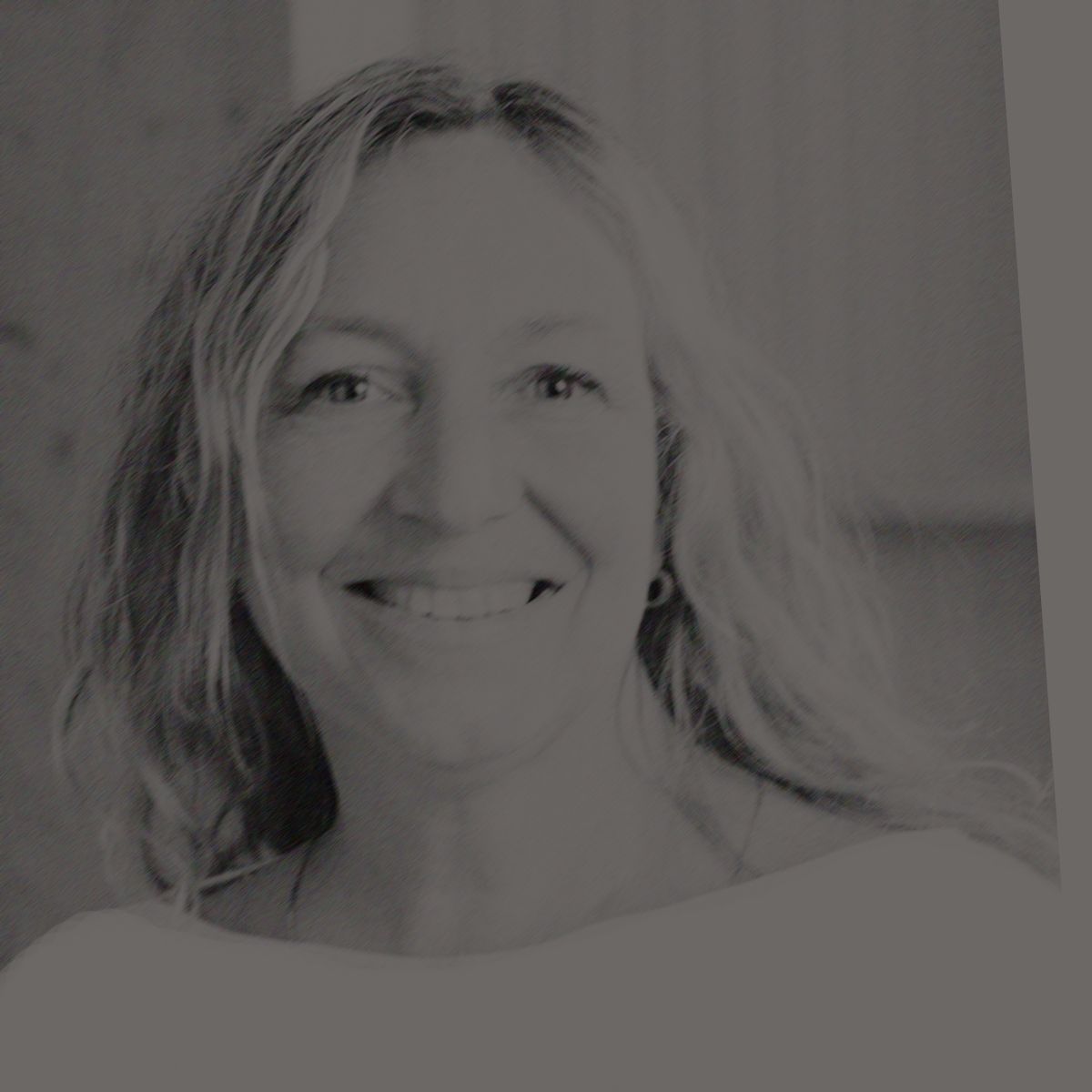 Femme aux longs cheveux blonds, souriante, vêtue d'une chemise blanche, à l'intérieur.