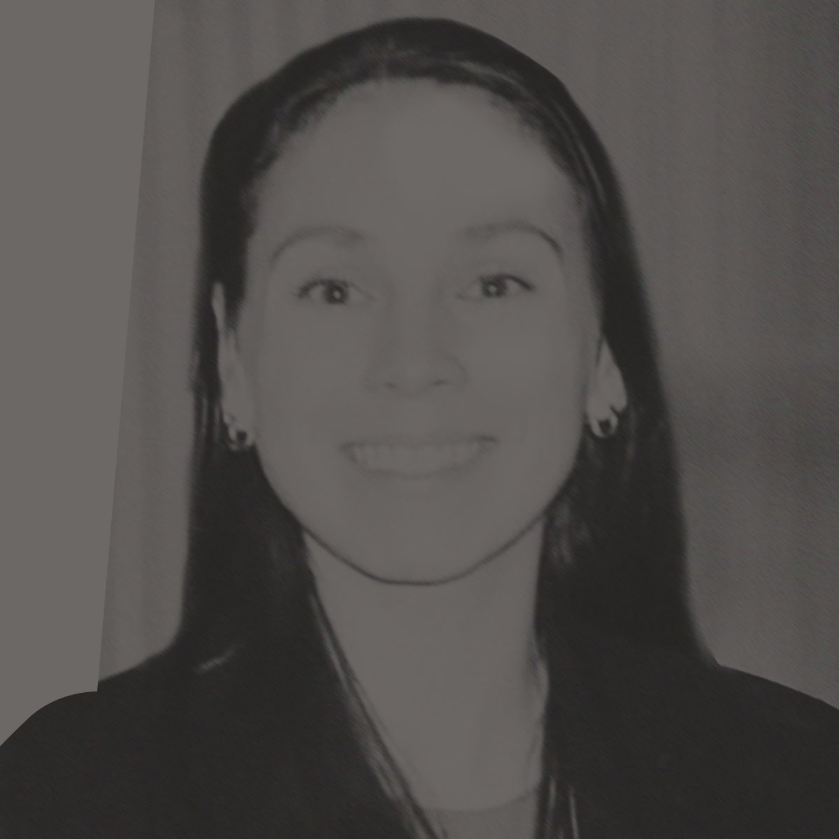 Une femme aux cheveux foncés sourit, vêtue d'un blazer noir et de boucles d'oreilles créoles dorées.