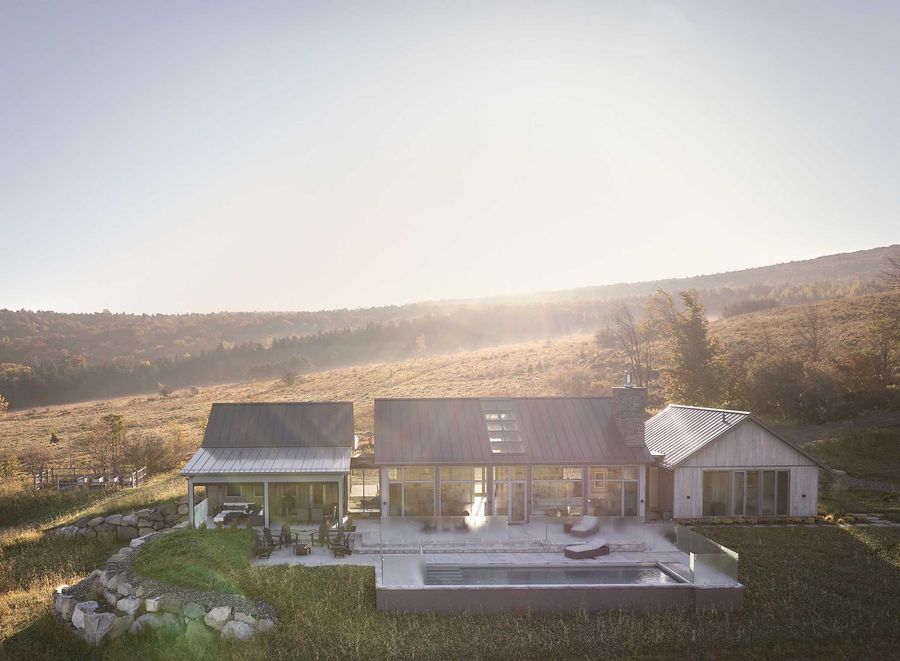 Maison moderne en noir et blanc avec une femme passant devant un abri de voiture par une journée ensoleillée.