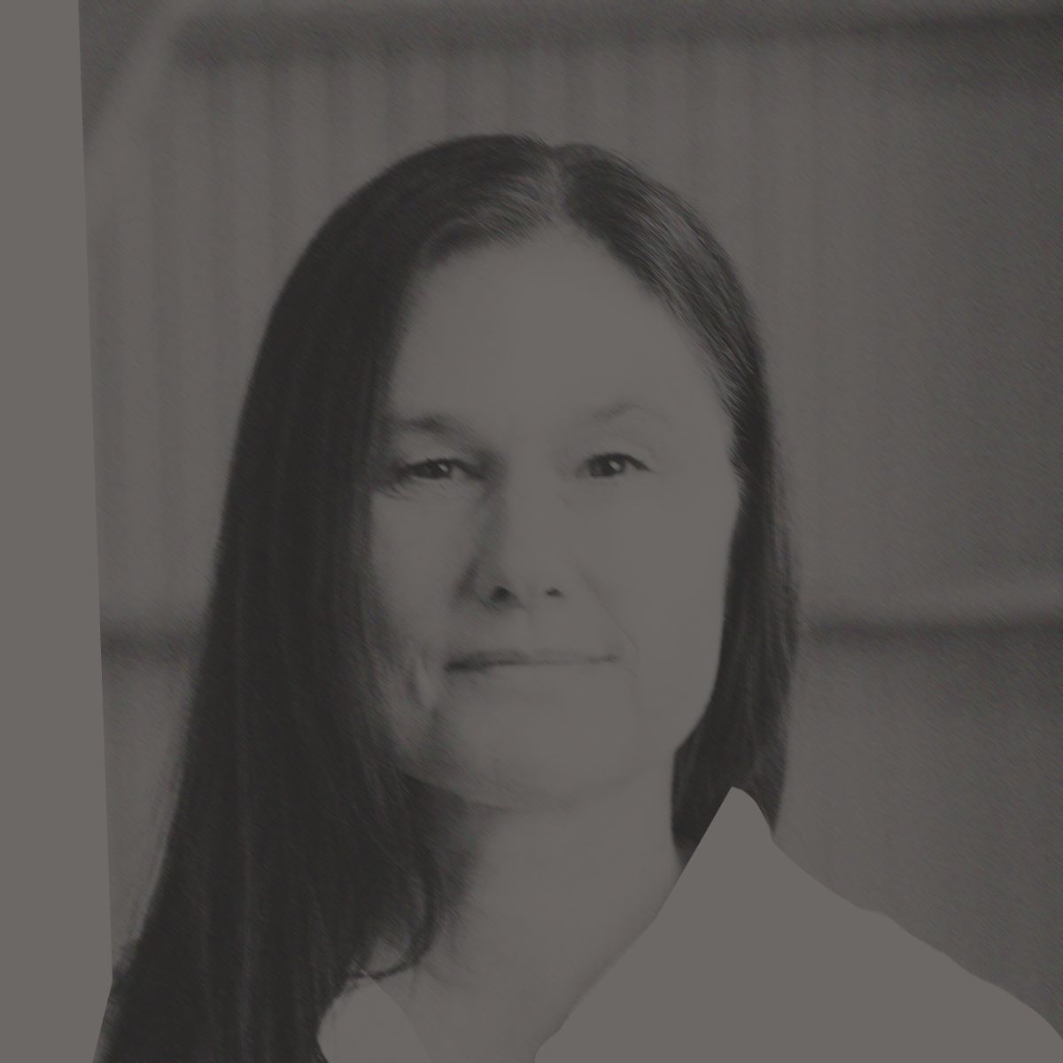 Une femme aux longs cheveux noirs, vêtue d'une chemise blanche, sourit devant un fond en bois.