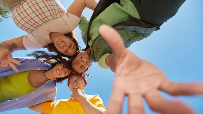 A group of people are standing in a circle and reaching out towards the camera.