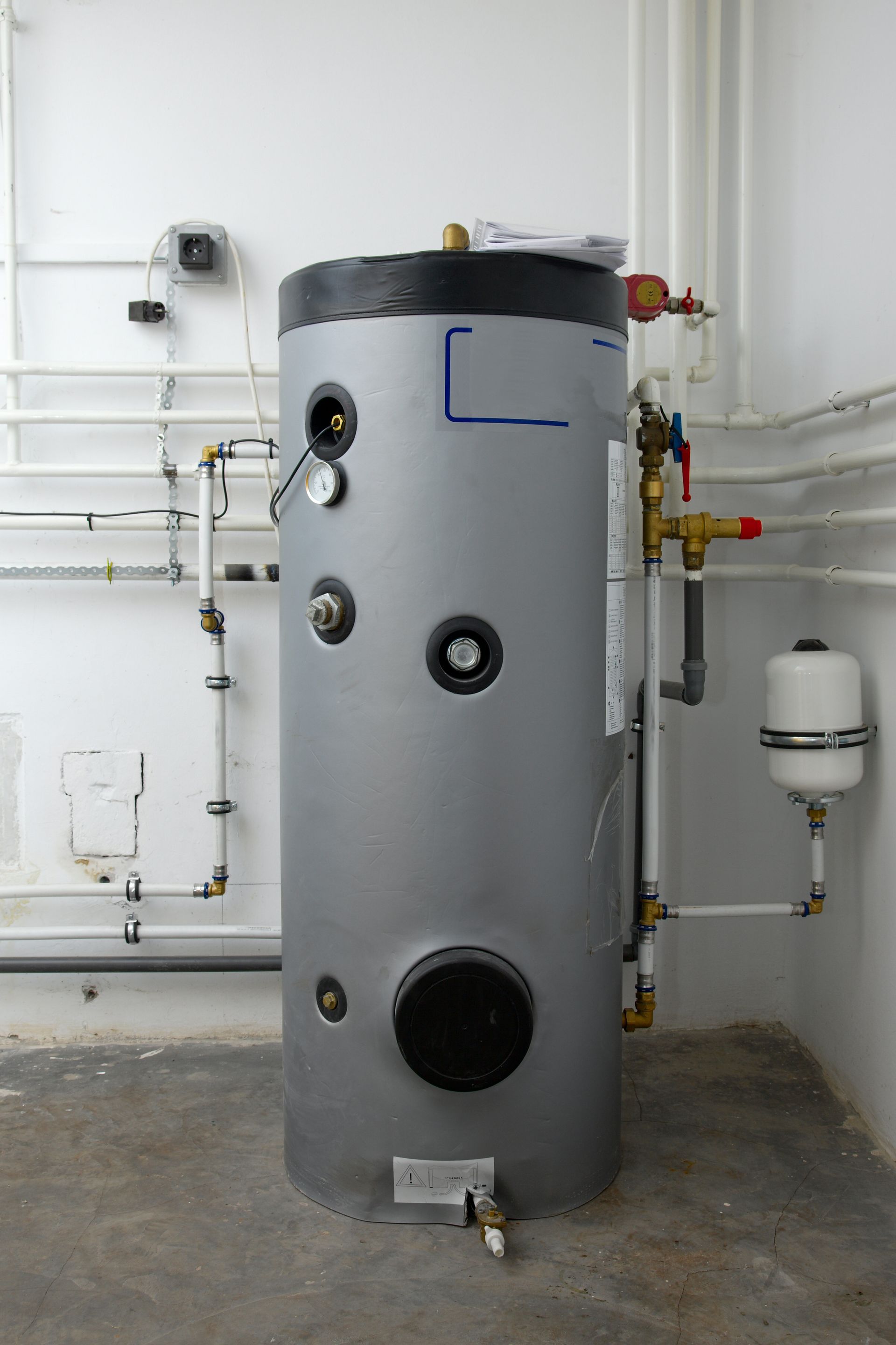 Silver water heater in a utility room, with pipes and connections visible.