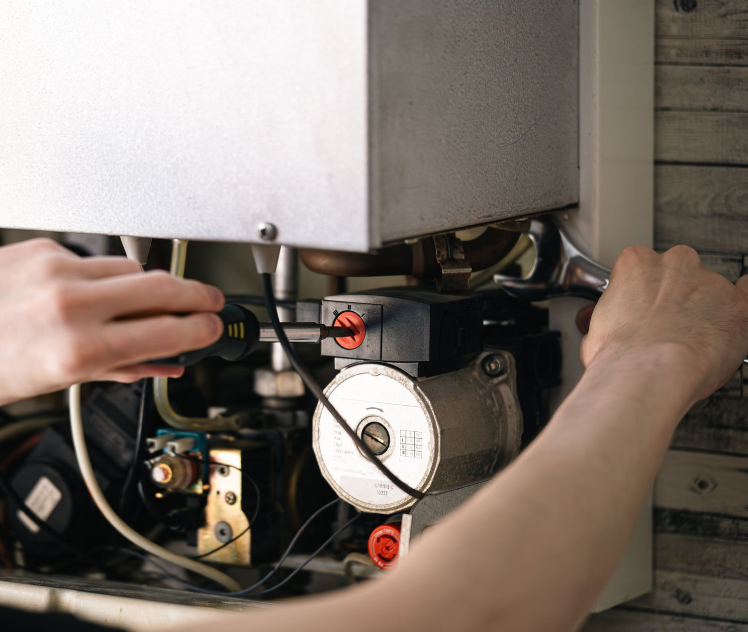 Person working on a heating system. Close-up of hands using tools to adjust components.