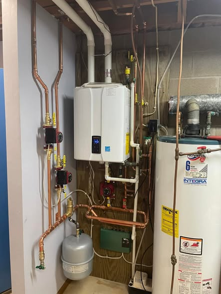 Gray furnace in a basement with silver ductwork and white pipes.
