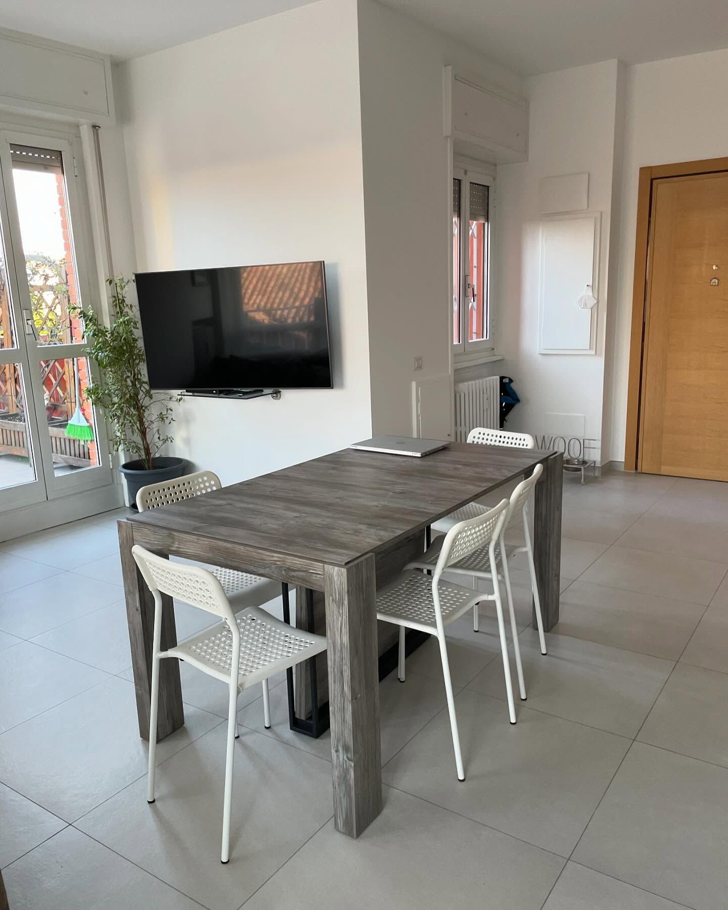 Un soggiorno con tavolo, sedie e TV a schermo piatto a parete.