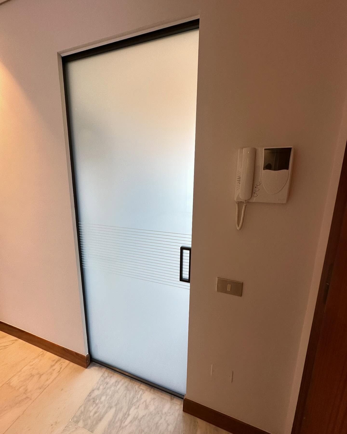 Una stanza con una porta scorrevole in vetro e un telefono sul muro.