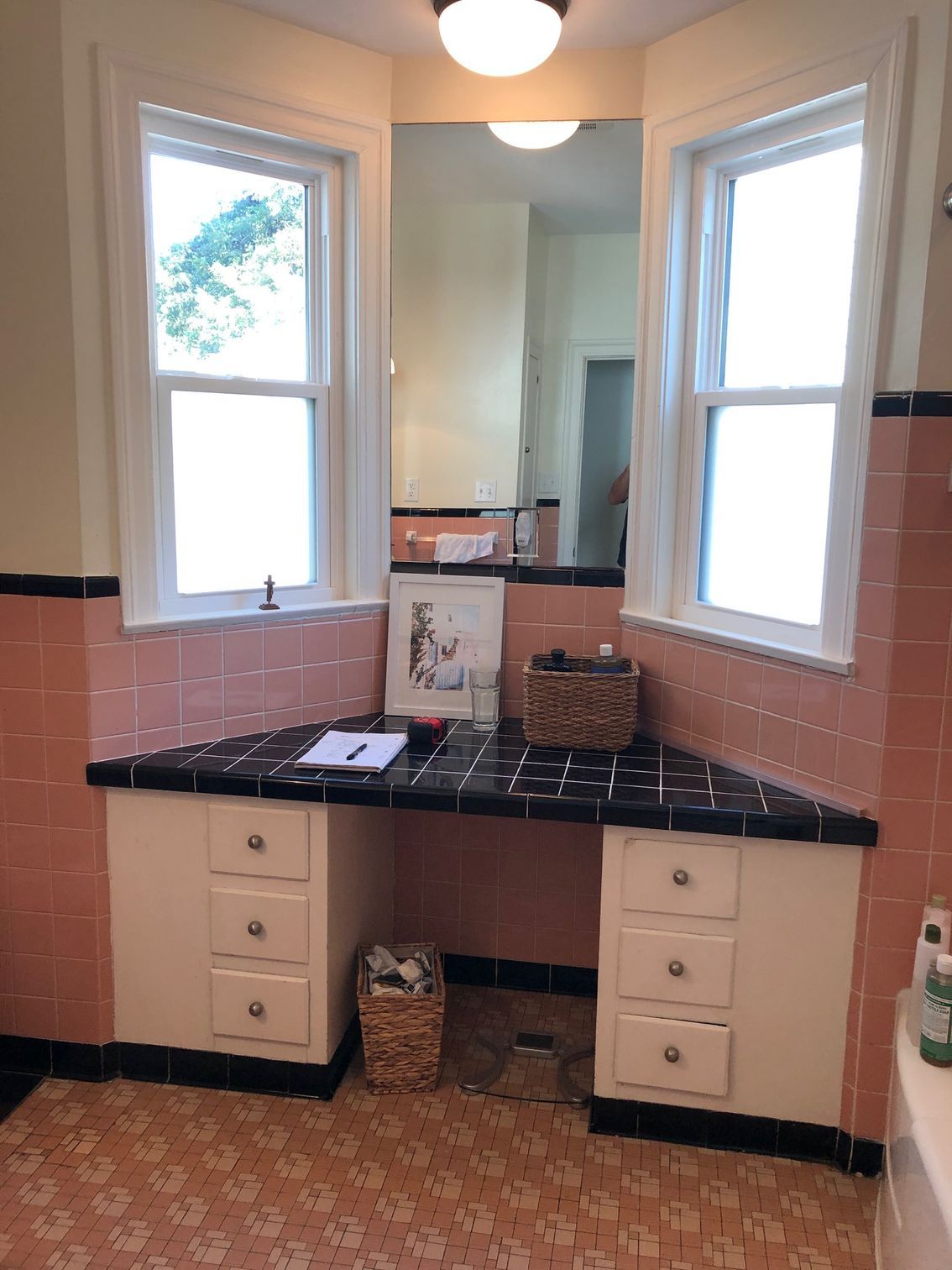 A bathroom with pink tiles , two sinks , a mirror and two windows.