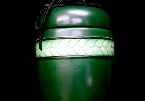 Green cylindrical container with a braided black cord and a white patterned band around the middle