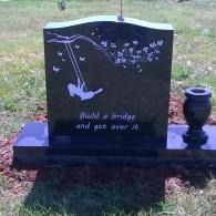 Black gravestone with a swing and butterflies, inscribed “Build a bridge and get over it.”
