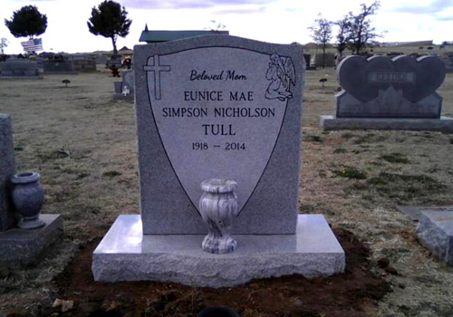 Gravestone in a cemetery with engraved name and dates, set on a concrete base.