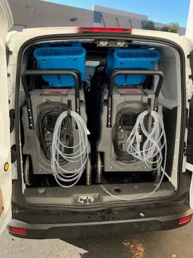 Two dehumidifiers loaded in the back of a white van, ready for water damage cleanup.