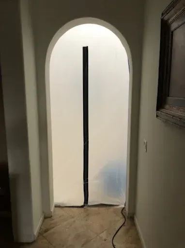 Arched doorway with a white plastic sheet covering it, sealed by a black zipper.