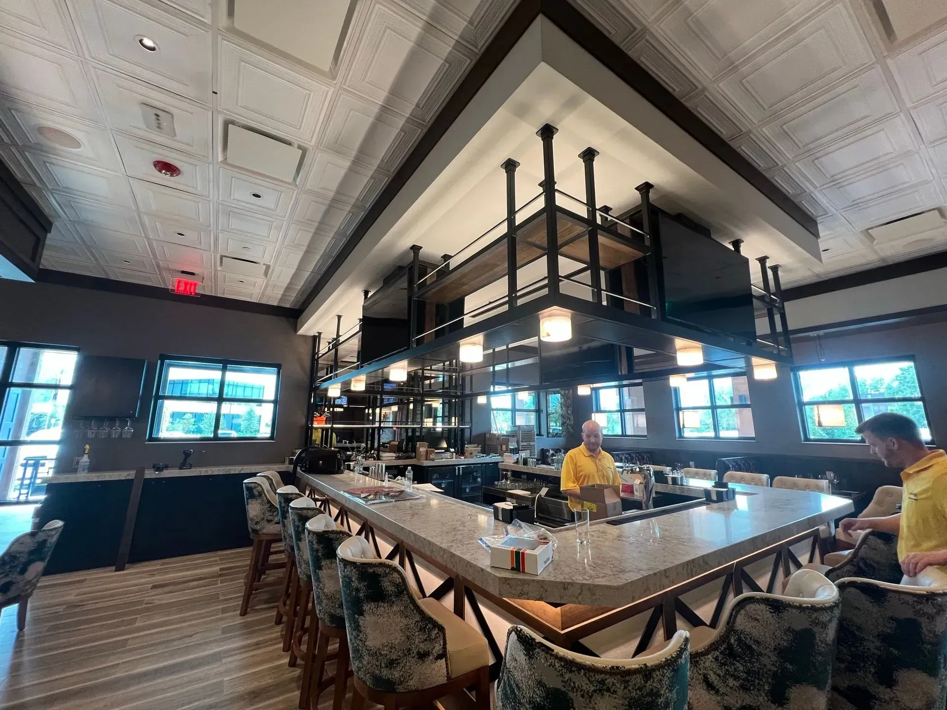 A man in a yellow shirt is sitting at a long bar in a restaurant.