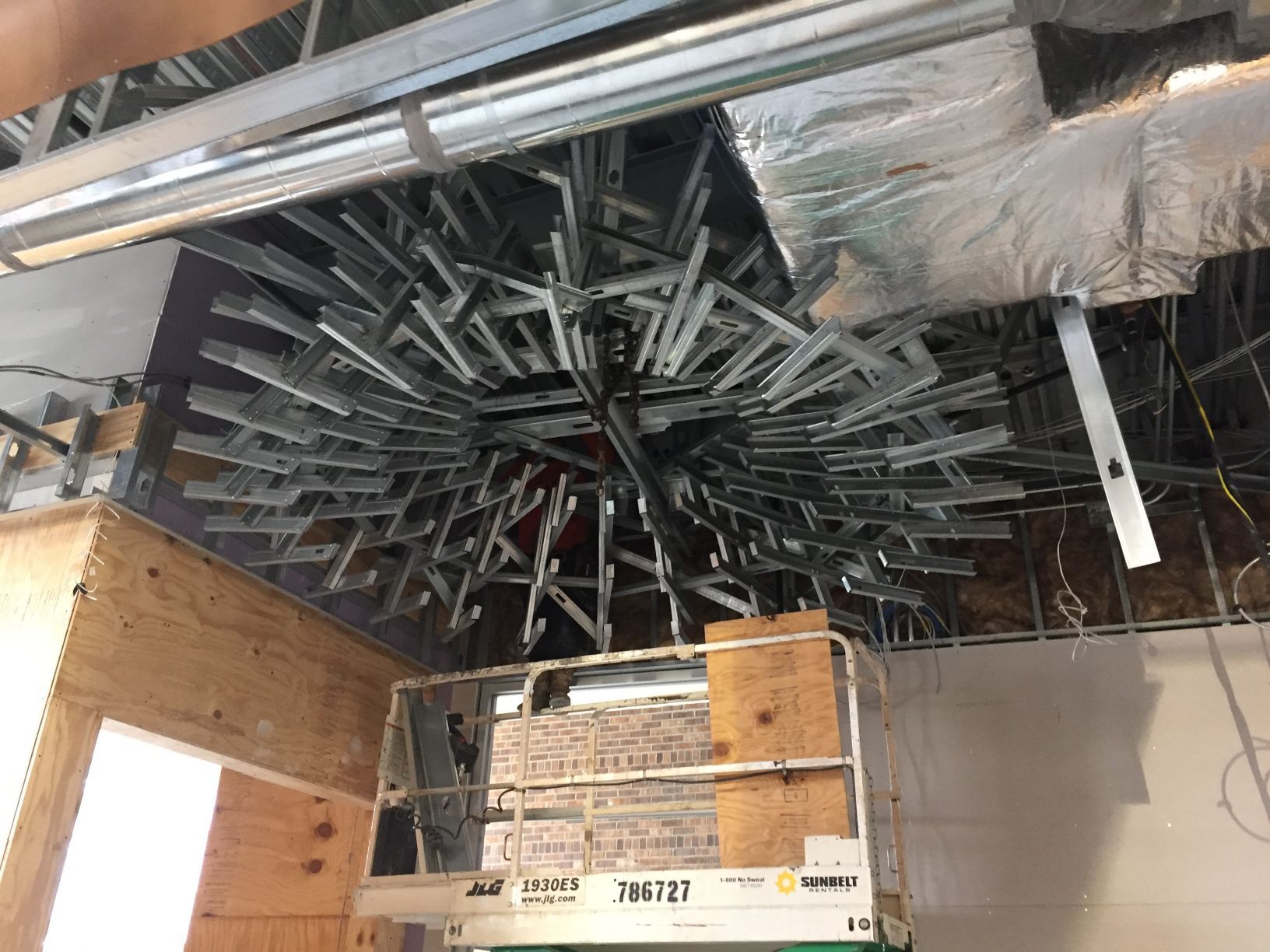 A person is standing on a ladder in a room with a ceiling that is being built.