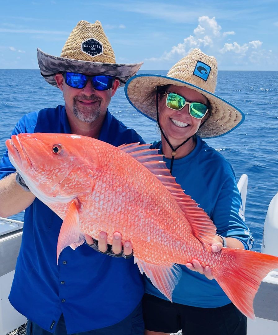 A man and a woman are holding a large red fish on a boat.