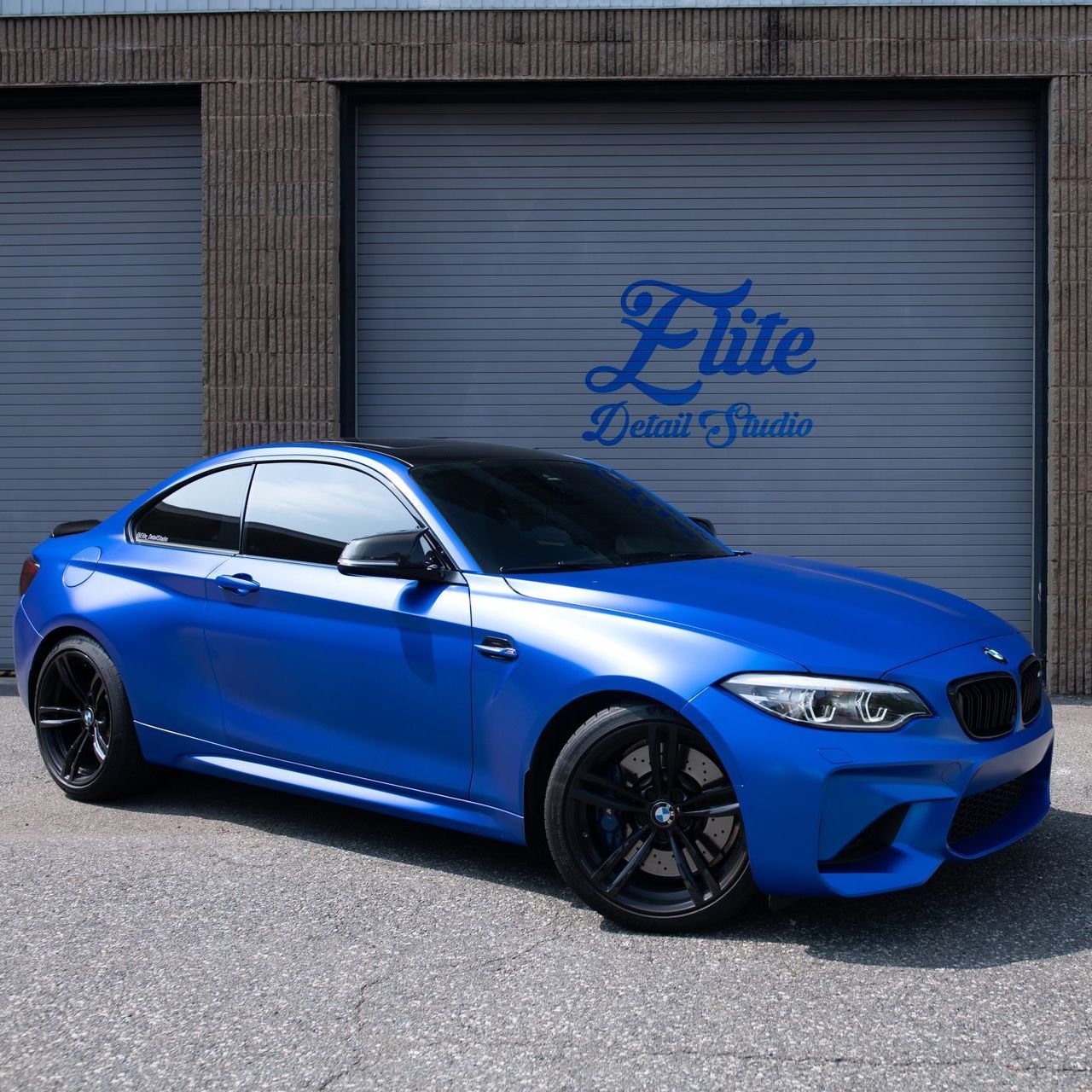 A blue car is parked in front of the elite detail studio