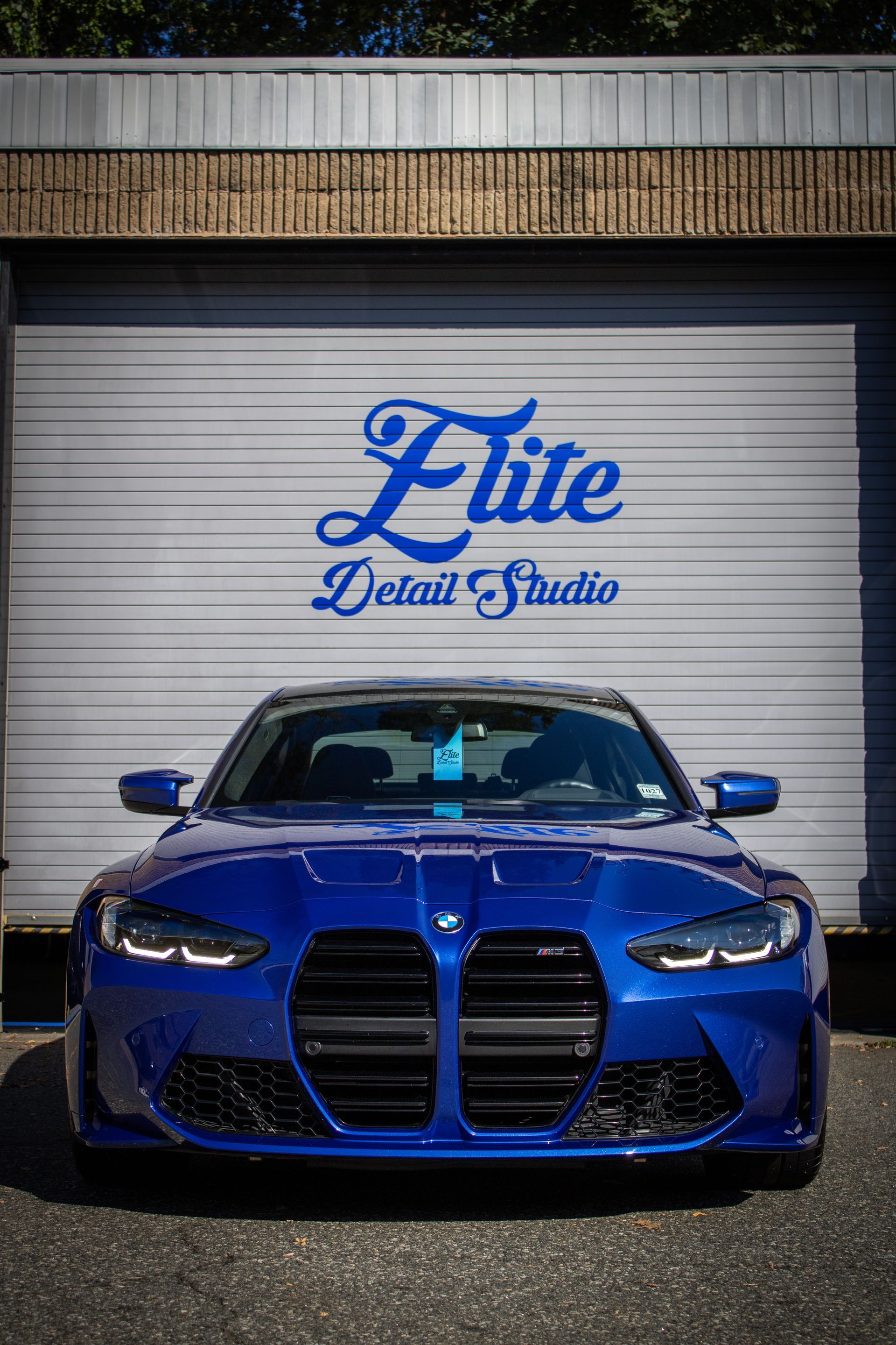 Blue BMW sedan parked in front of an Elite Detail Studio garage door.