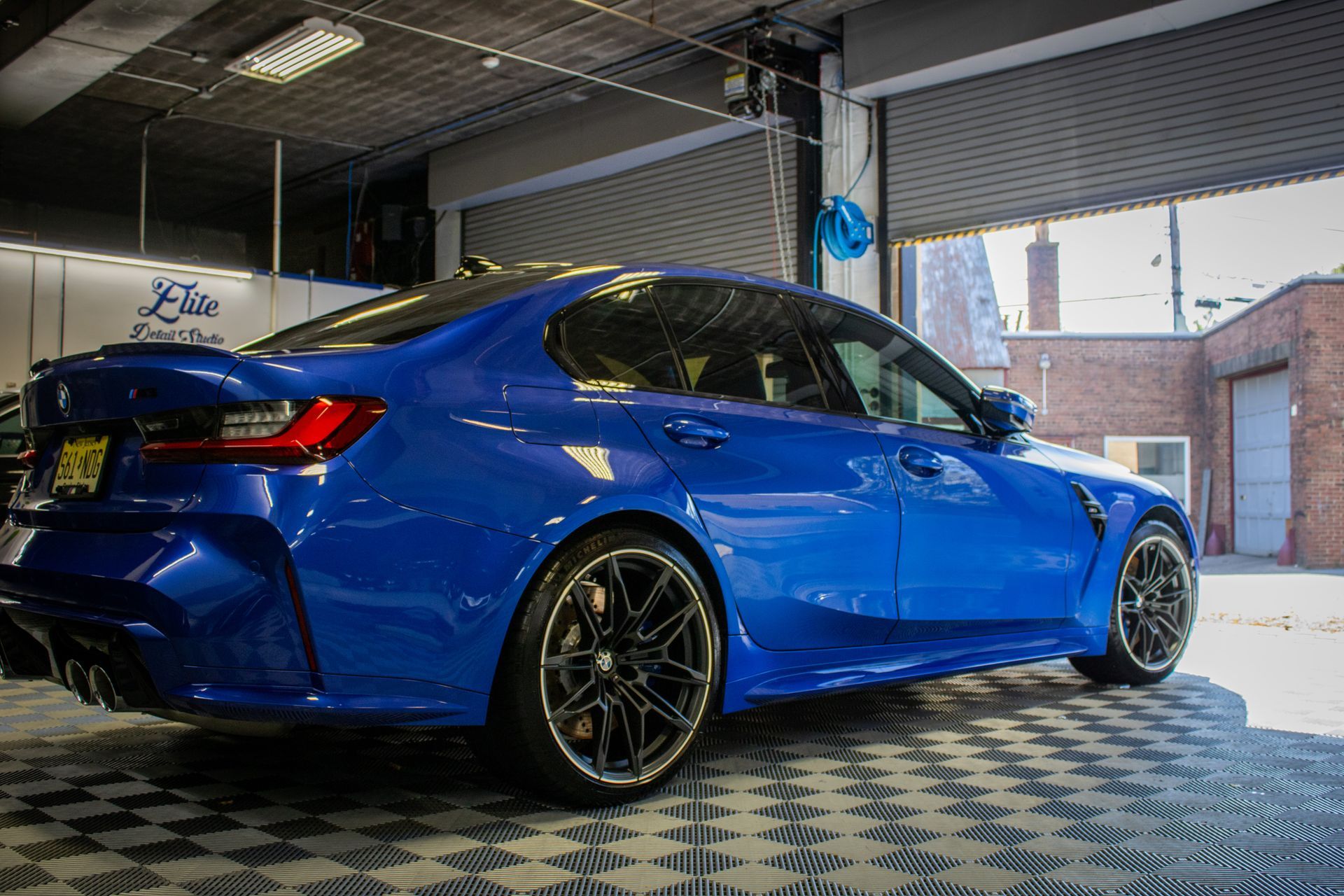 Blue sports sedan in a garage, viewed from the rear side with custom black rims.