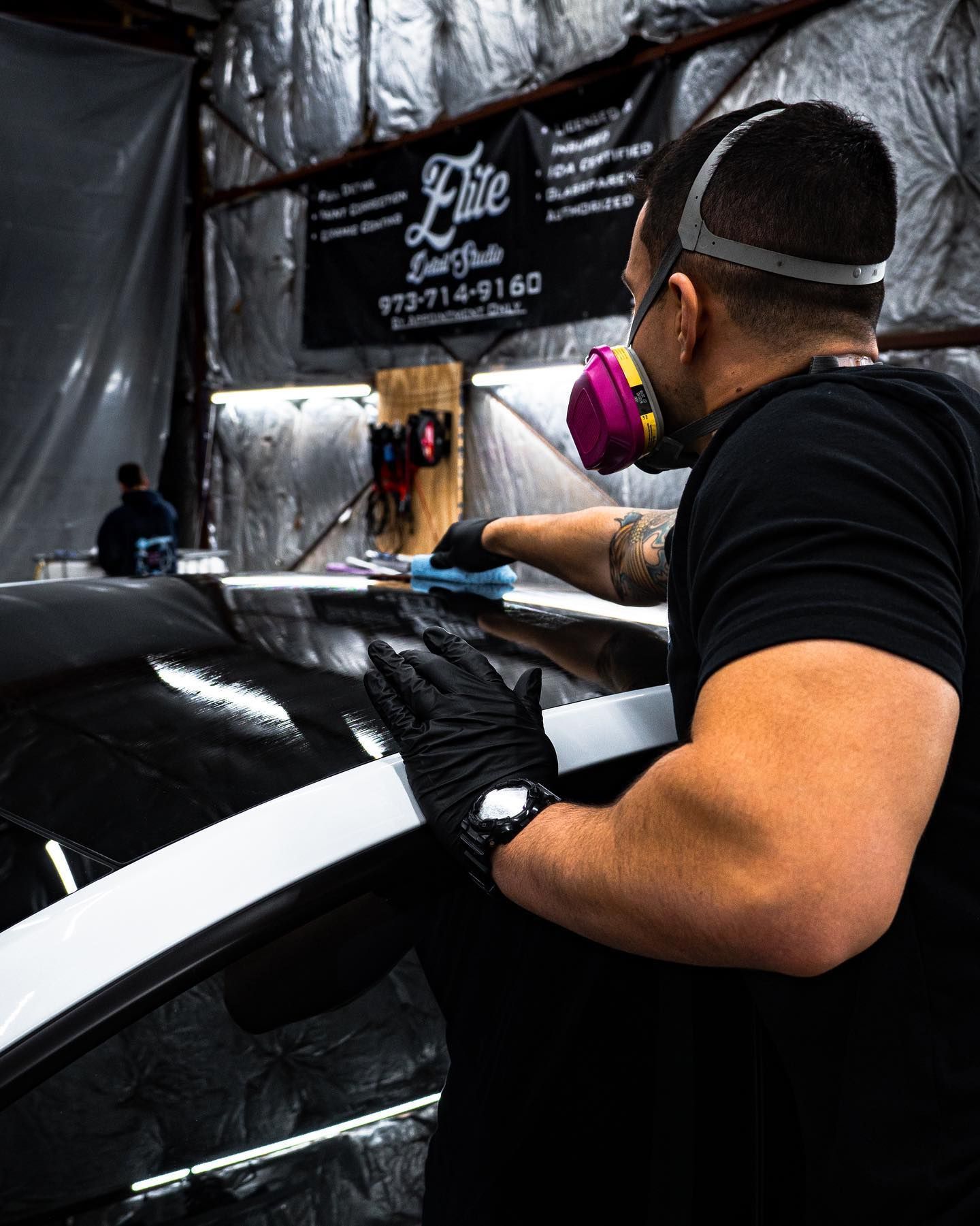 A man wearing a mask and gloves is working on a car