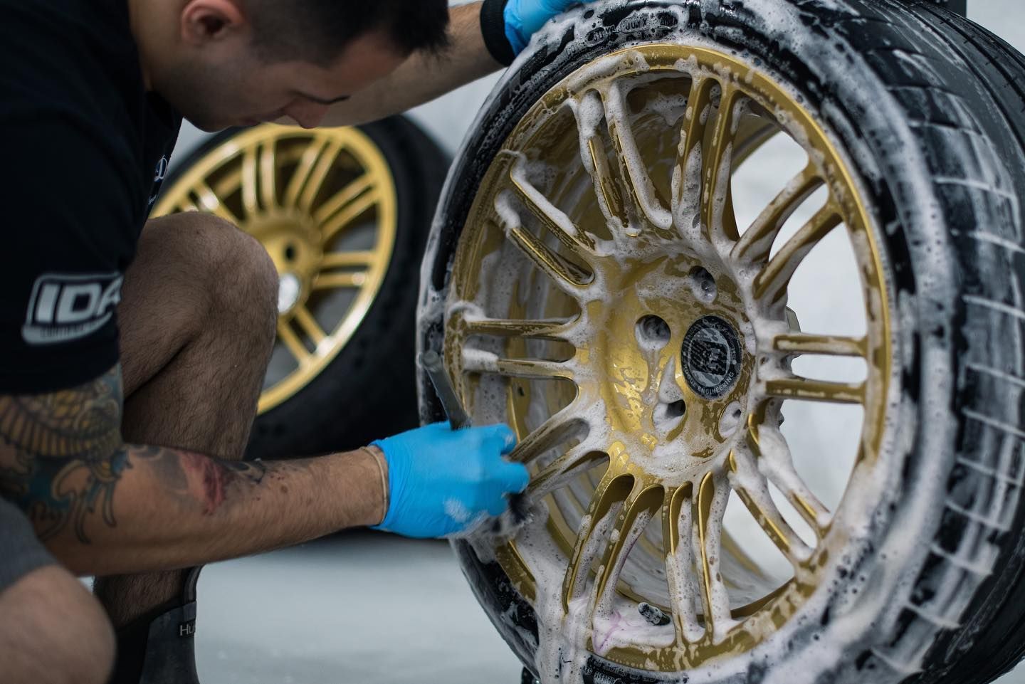 A man is cleaning a wheel with soap and a brush.