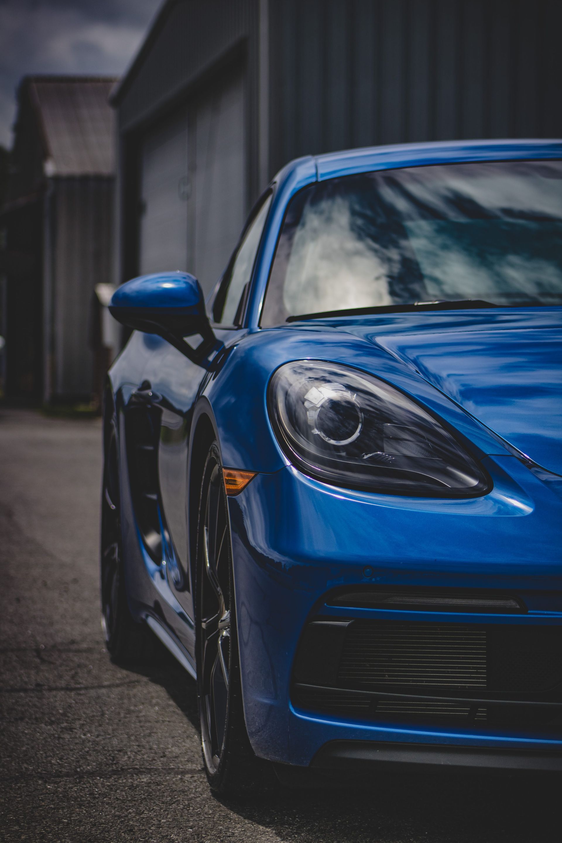 Blue sports car parked beside a building, front-left view with reflections on the hood.
