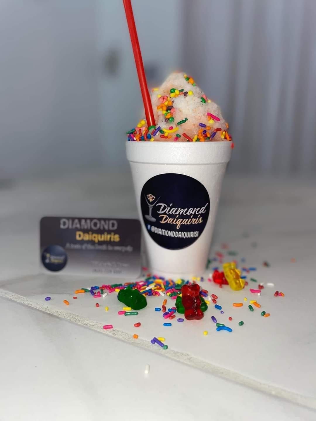 A cup of ice cream with sprinkles and gummy bears on a table.