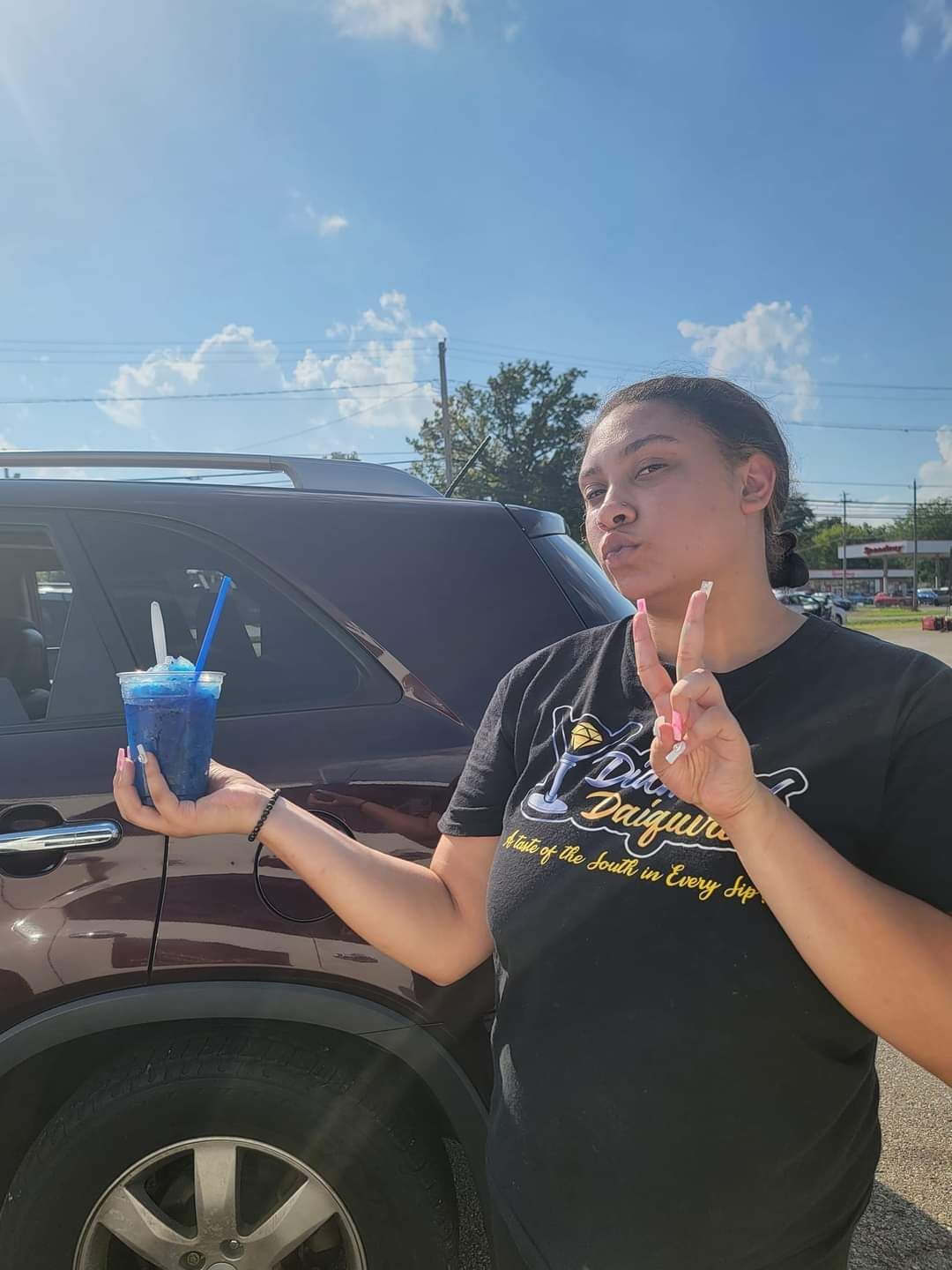 A woman is holding a cup of blue liquid in front of a car.