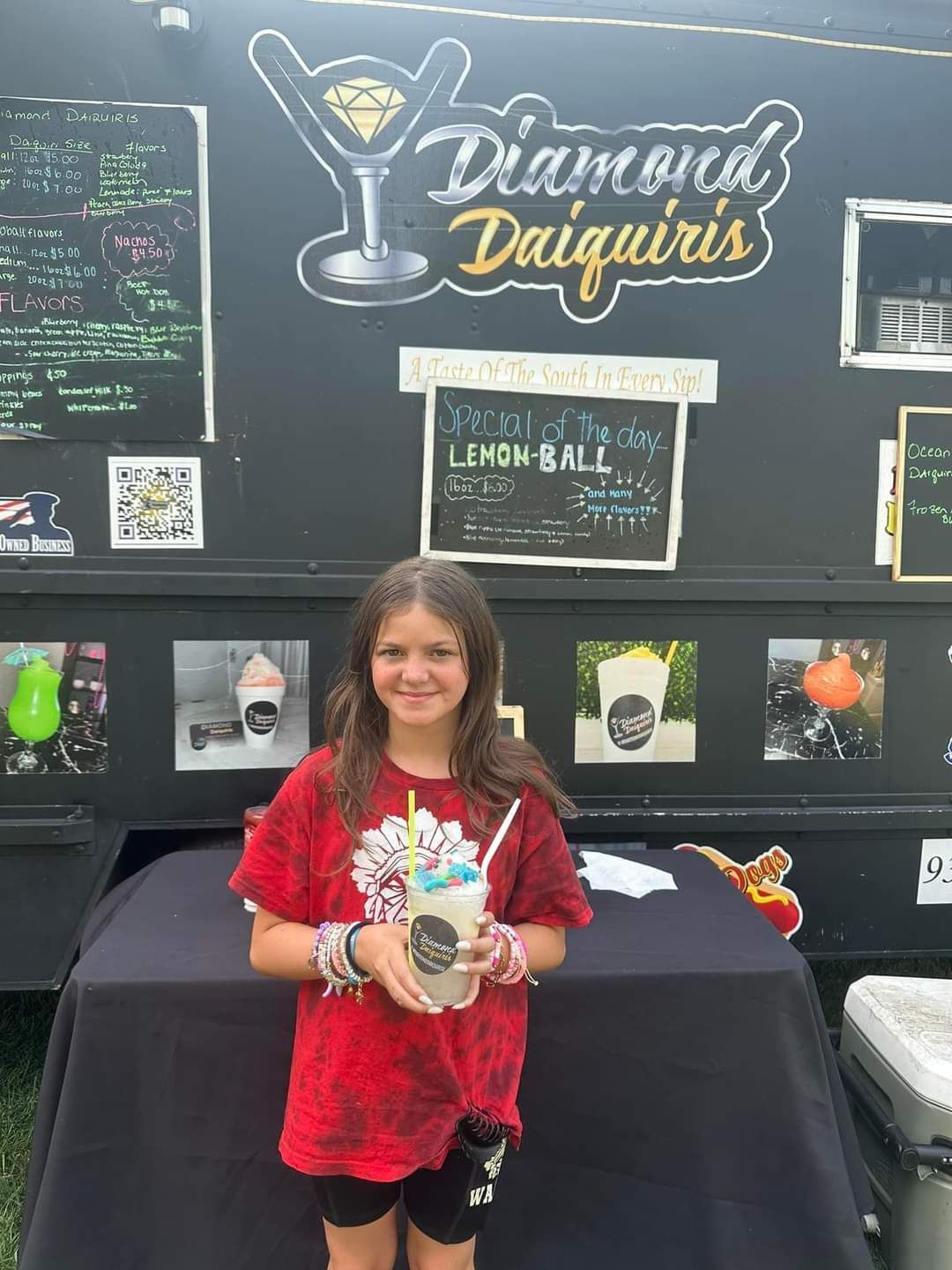 A young girl is holding a cup of ice cream in front of a food truck.