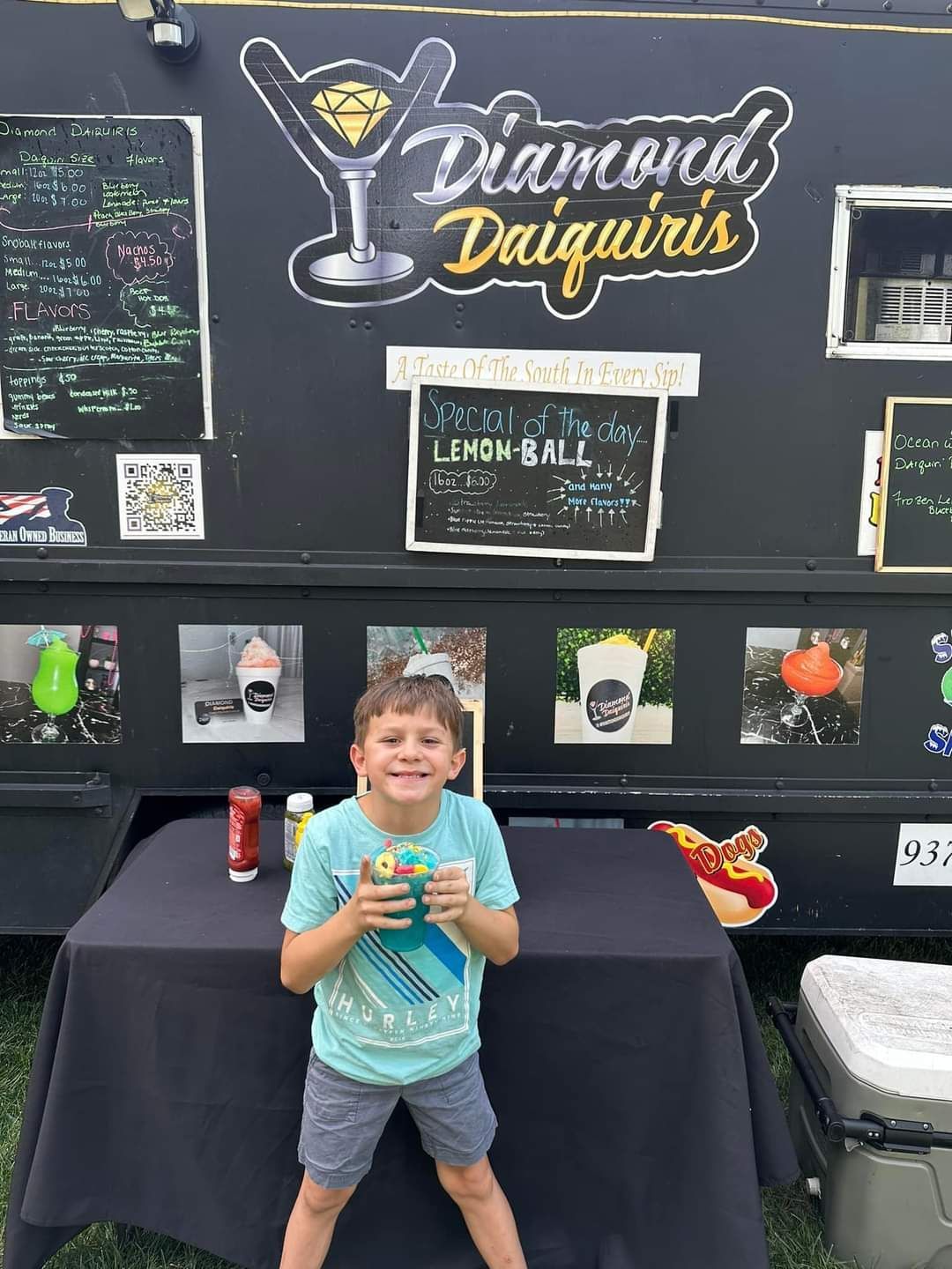 A young boy is standing in front of a table holding a drink.