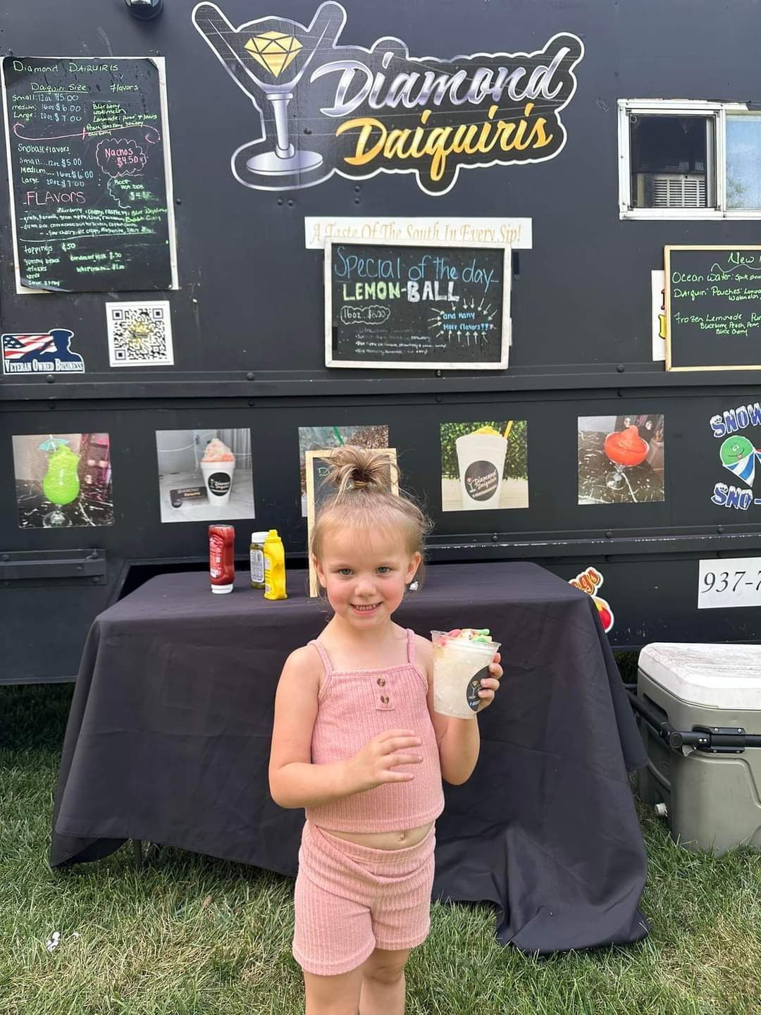 A little girl is standing in front of a food truck holding a drink.