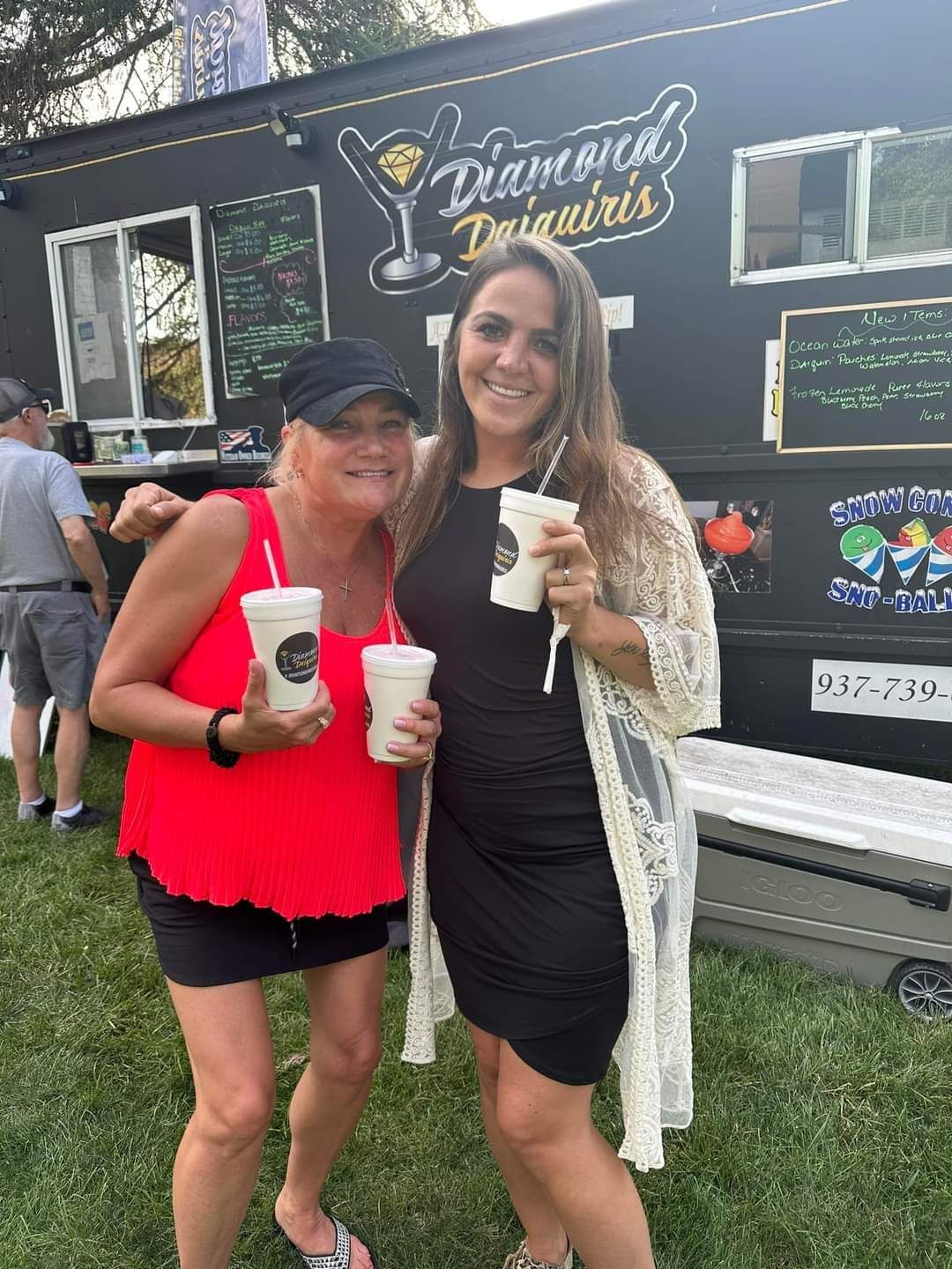 Two women are standing next to each other holding drinks in front of a food truck.
