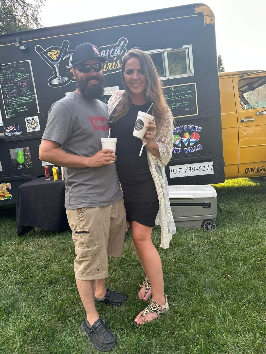 A man and a woman are standing next to each other in front of a food truck.