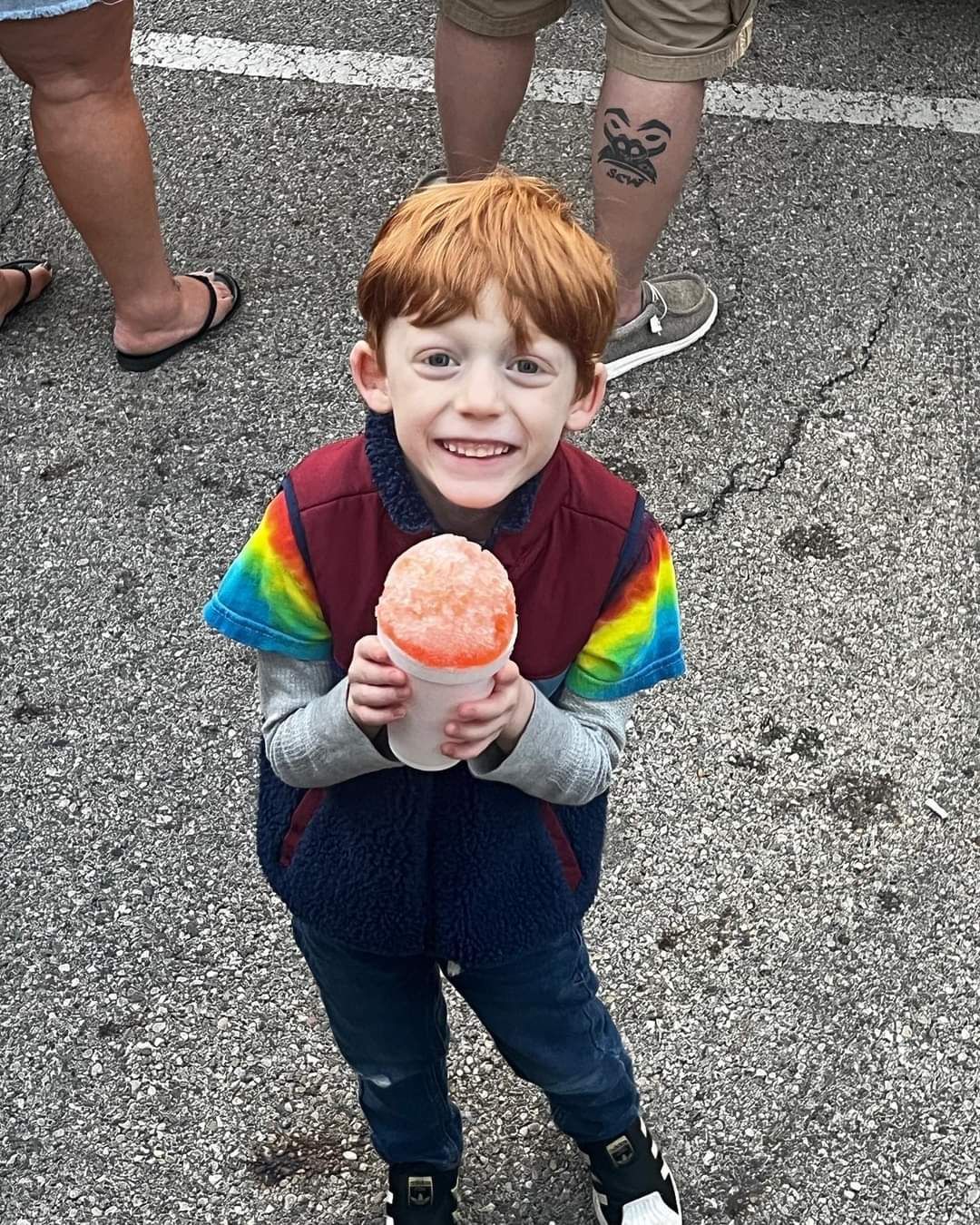 A young boy is holding a cup of ice cream and smiling.