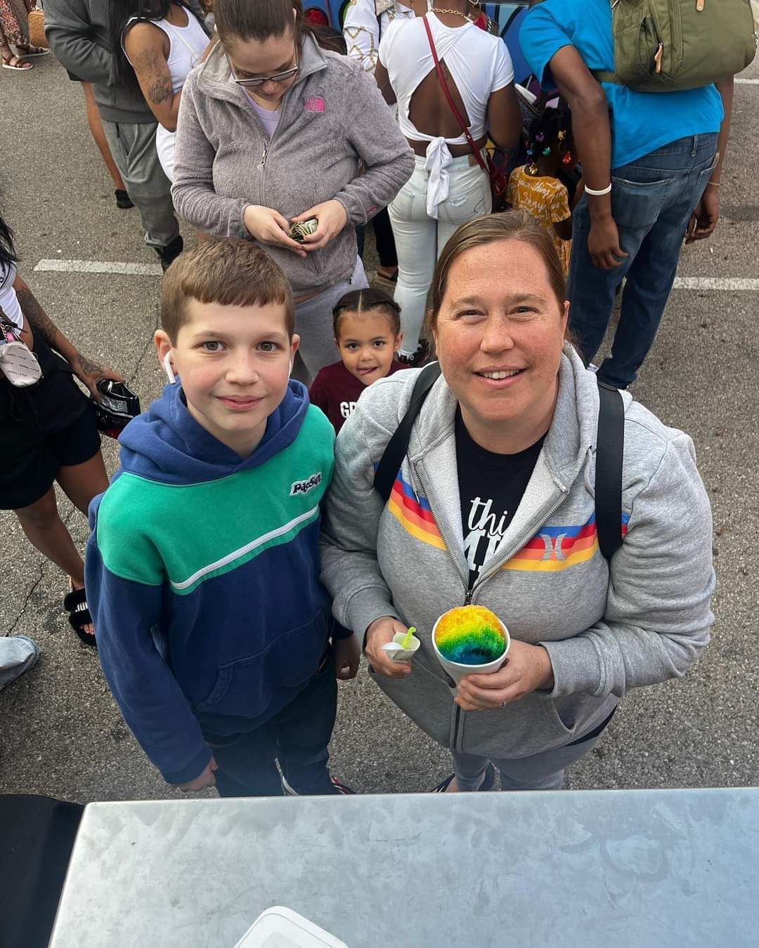 A woman is standing next to a boy holding a cup of ice cream.