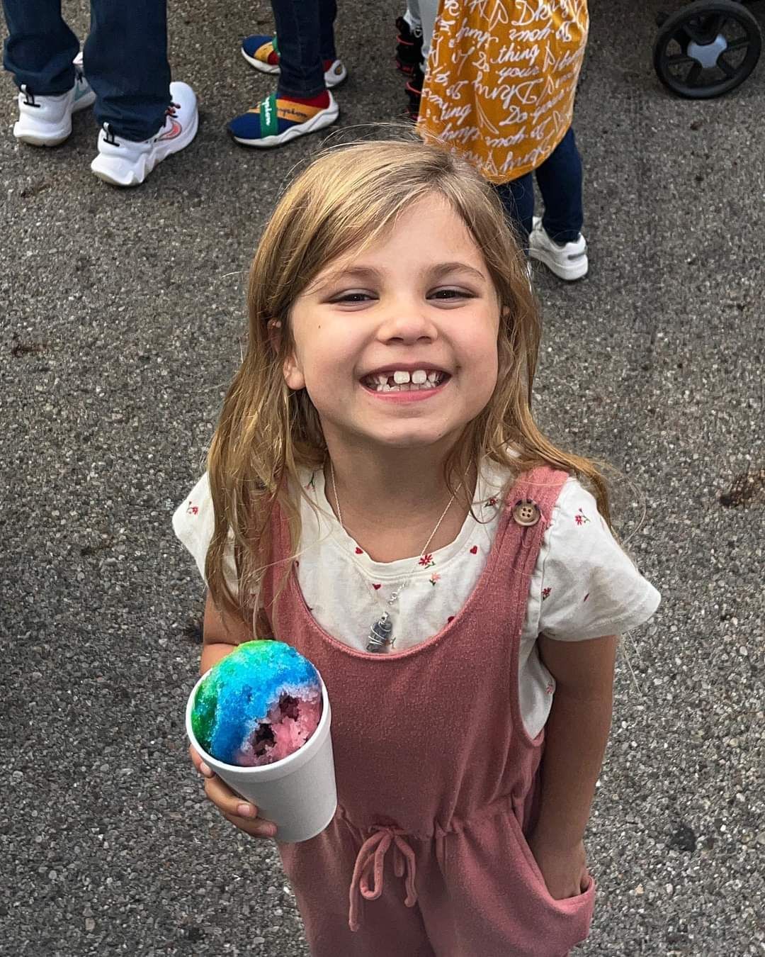 A little girl is holding a cup of ice cream and smiling.