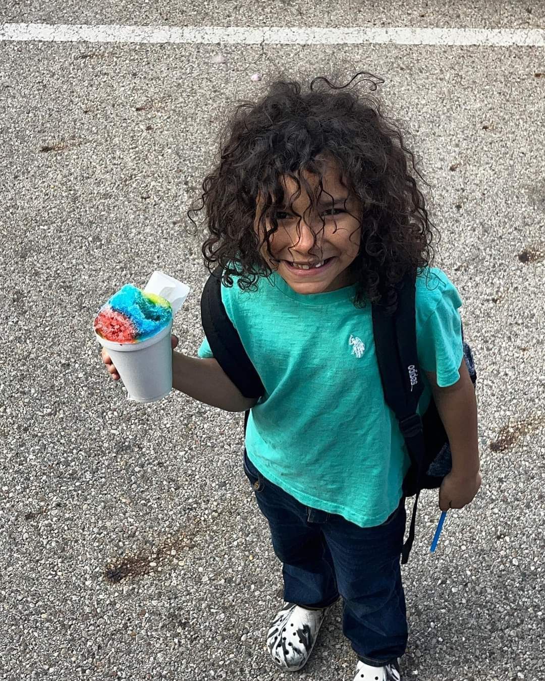 A young boy with curly hair is holding a cup of ice cream.