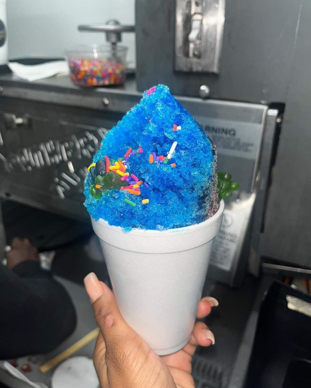 A person is holding a cup of blue ice cream with sprinkles