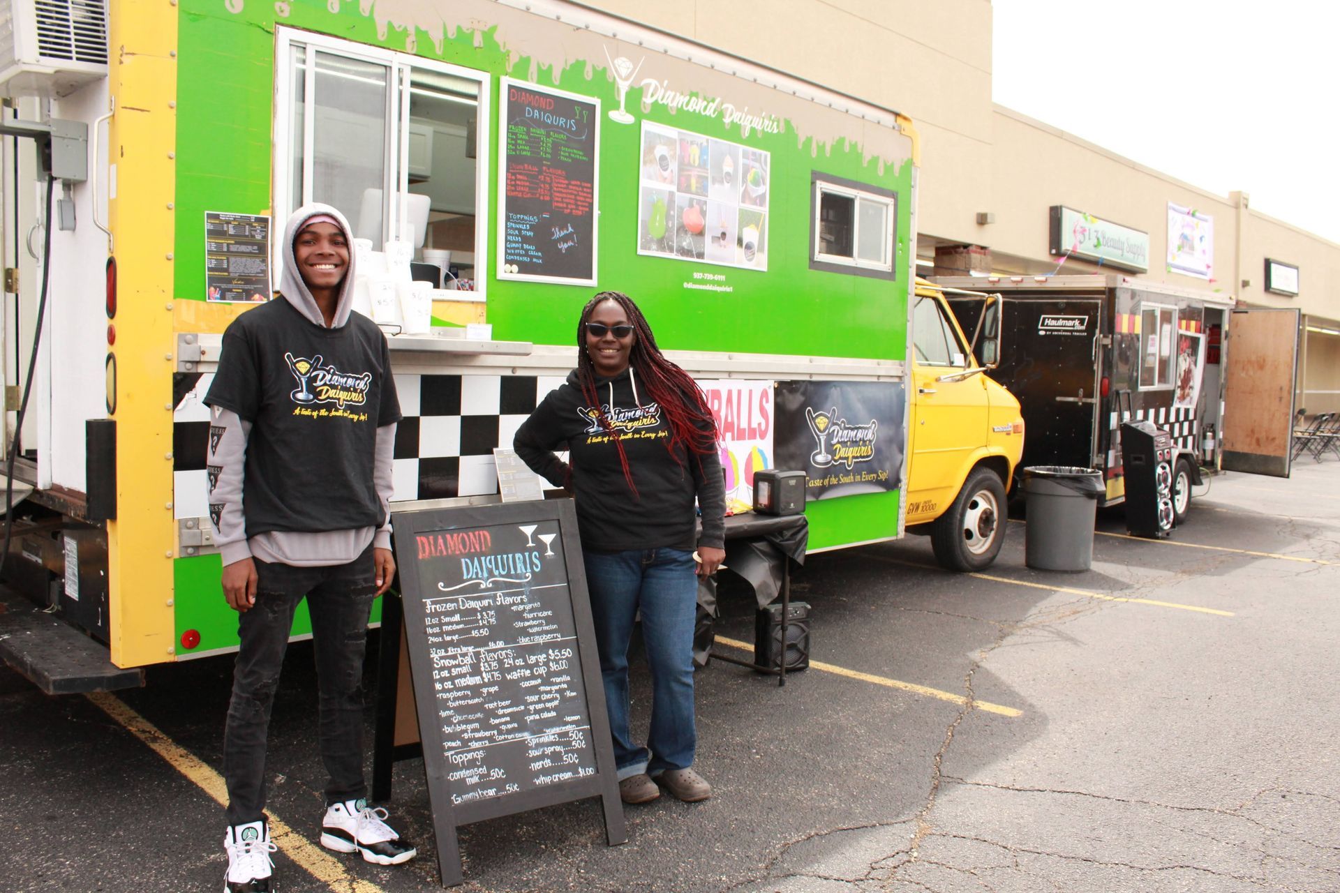A man and a woman are standing in front of a food truck.